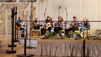Mehrere Jugendliche Personen und eine weitere Frau spielen in der Kirche zusammen Gitarre | © Don Bosco Berufsfachschule für Kinderpflege