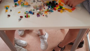 Mehrere Personen sitzen an einem Tisch der voll mit Legosteinen ist und bauen etwas damit | © Caritas Don Bosco Berufsfachschule für Kinderpflege